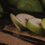 Close-up of sliced green pears on burlap cloth with knife, creating a rustic and fresh aesthetic.